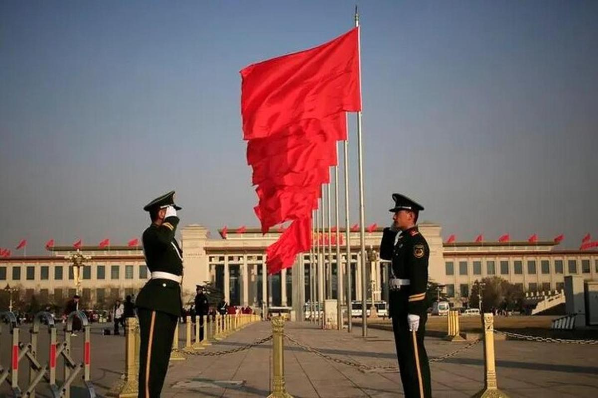 两名身穿制服的男子站在一栋挂着红旗的建筑物前