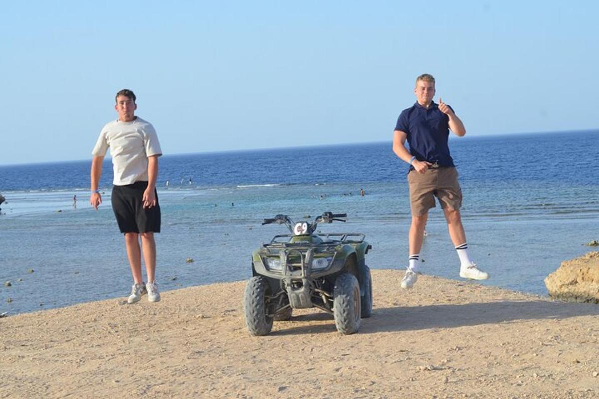 Dos hombres de pie en la playa con un vehículo todo terreno en la playa
