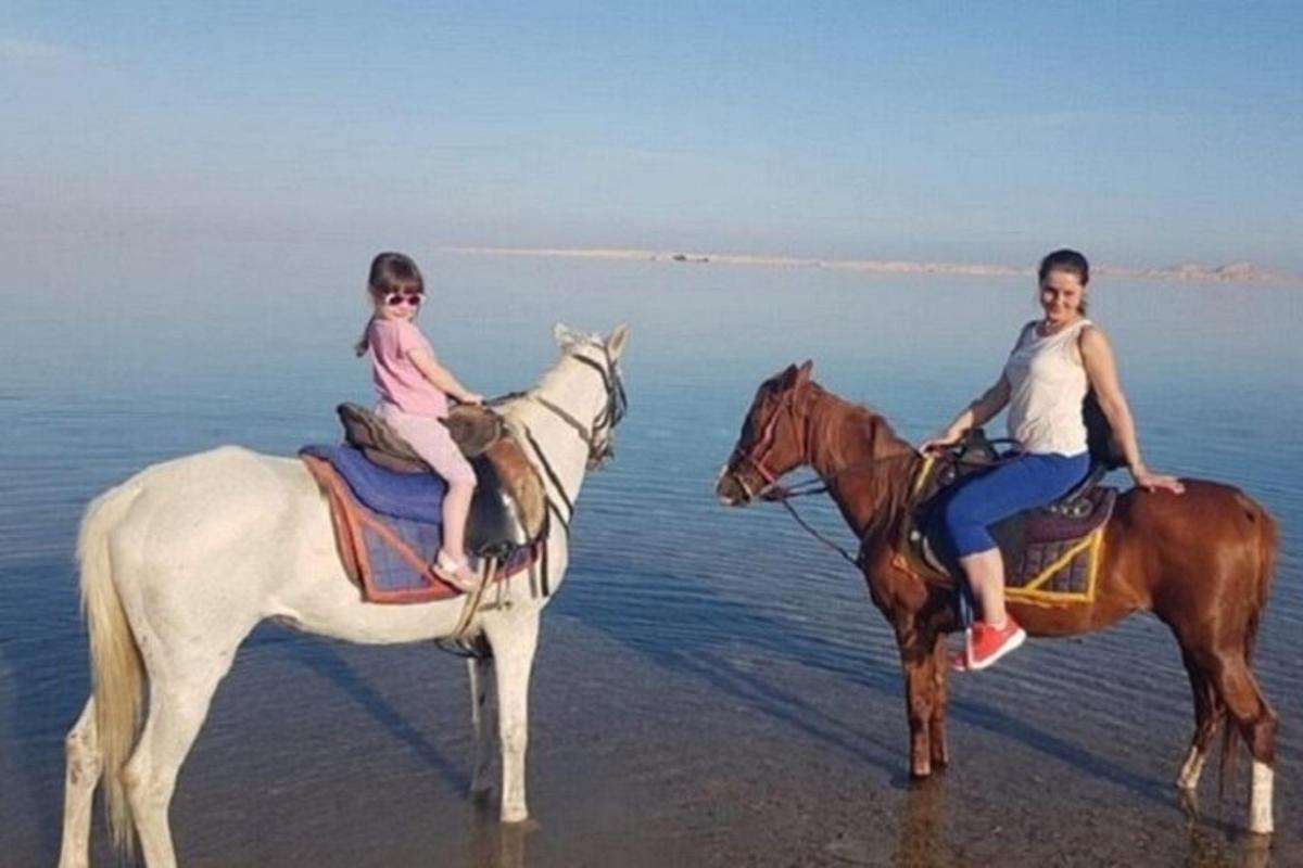 uma mulher e uma criança andando a cavalo na praia