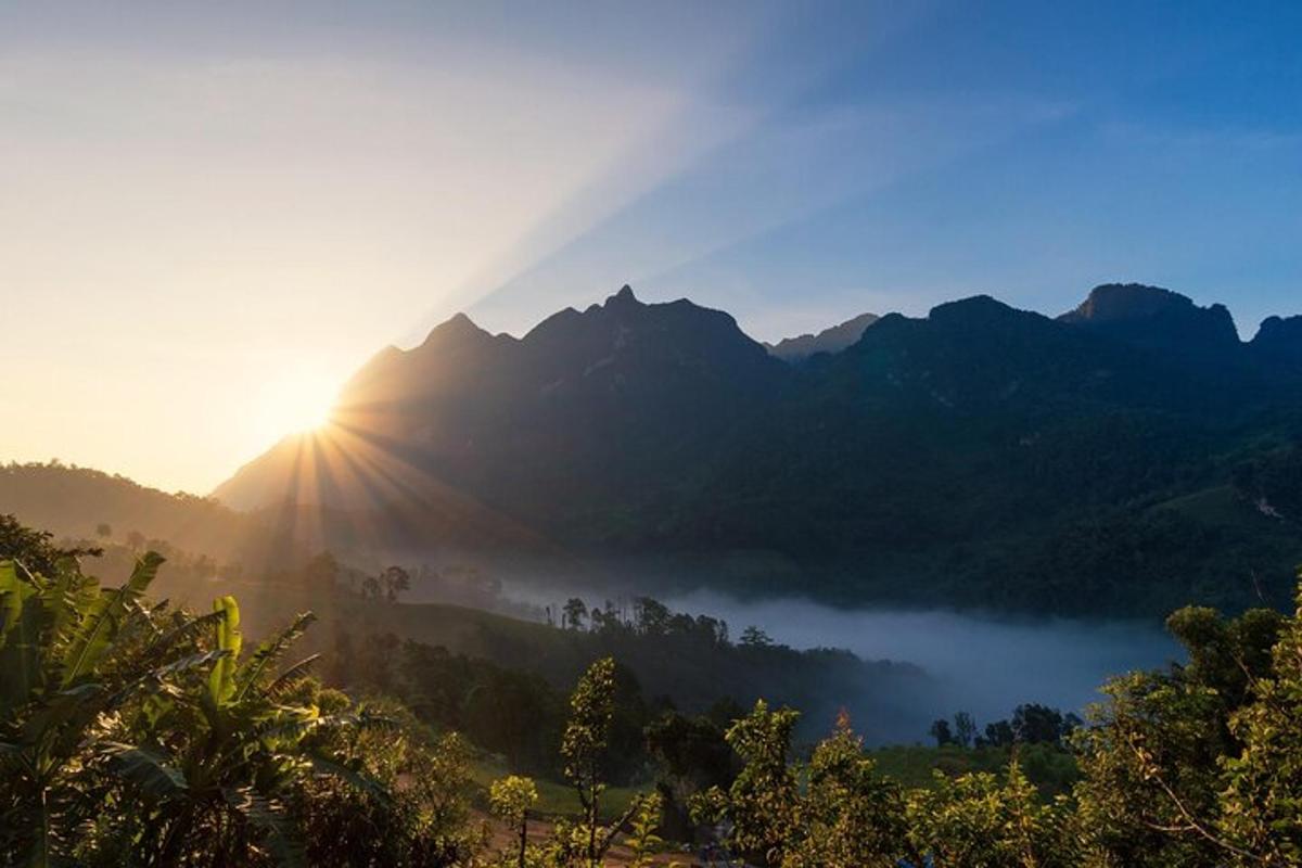 una vall ennuvolada amb el sol brillant a les muntanyes