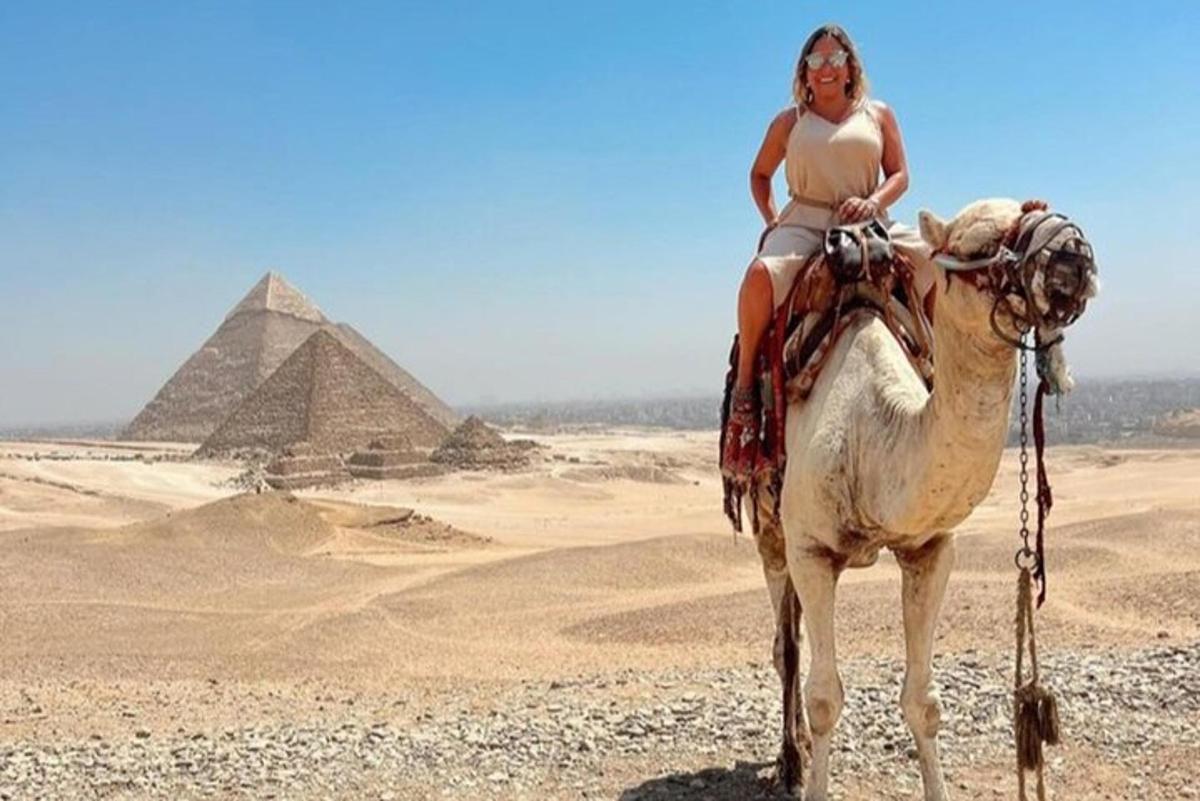 uma mulher montando um camelo em frente às pirâmides
