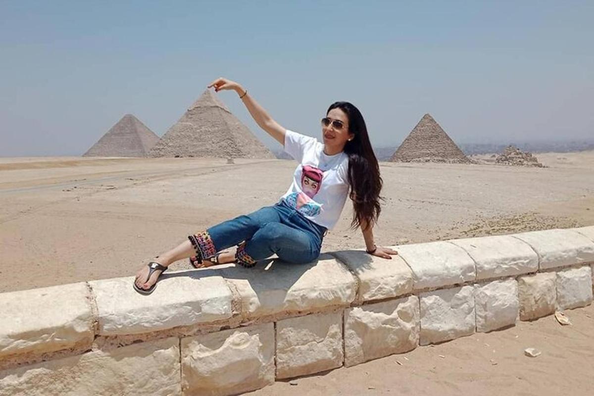 uma mulher sentada em um muro em frente às pirâmides