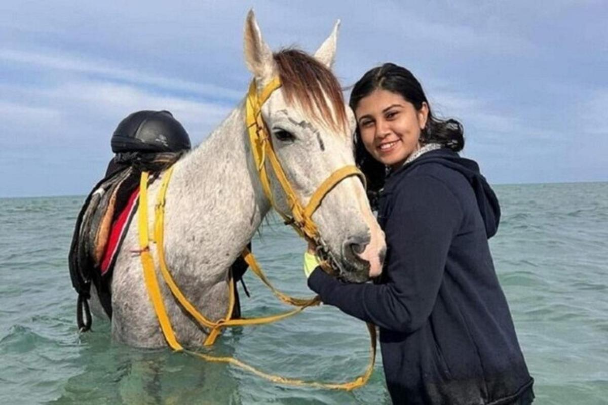 žena stojící vedle koně v oceánu