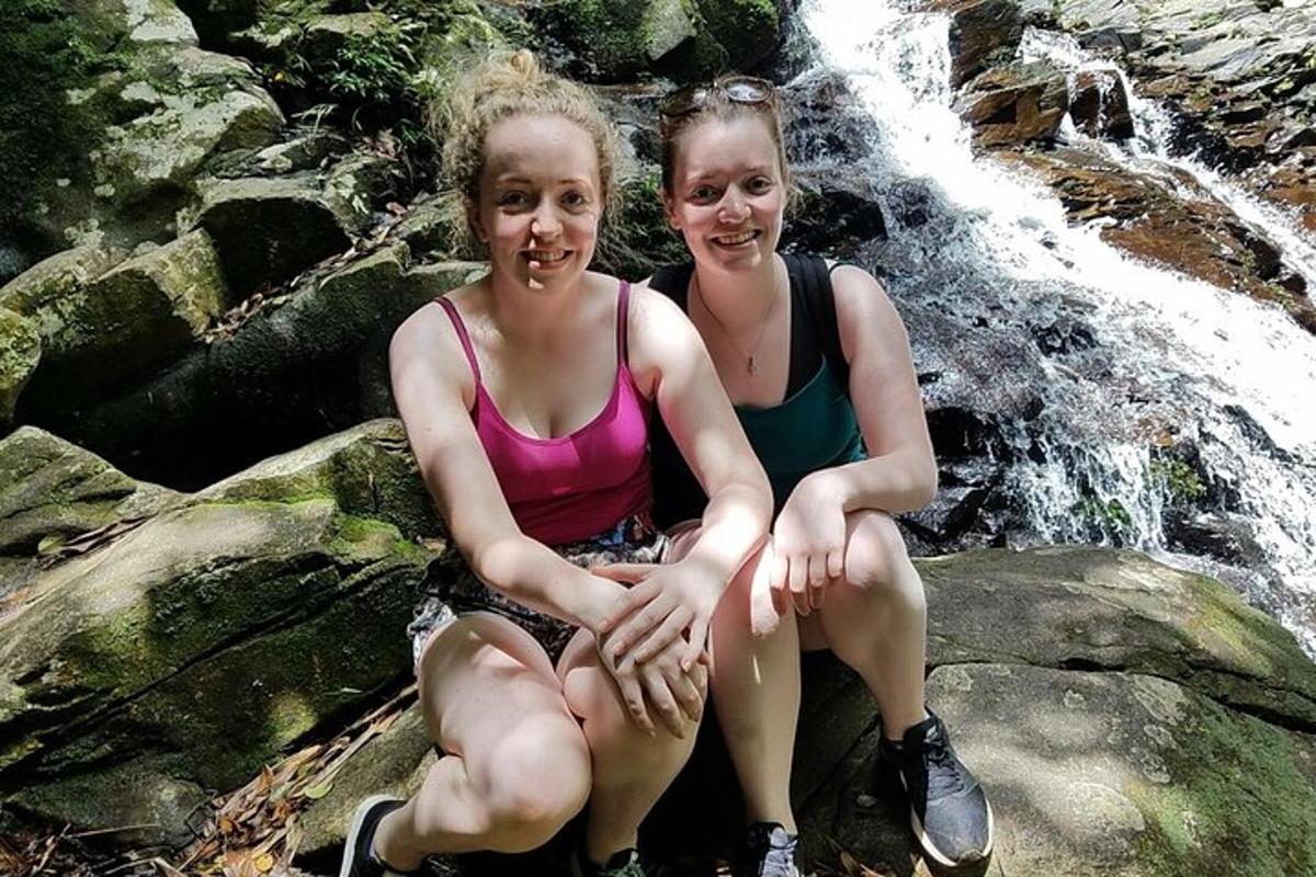 duas meninas sentadas em pedras em frente a uma cachoeira
