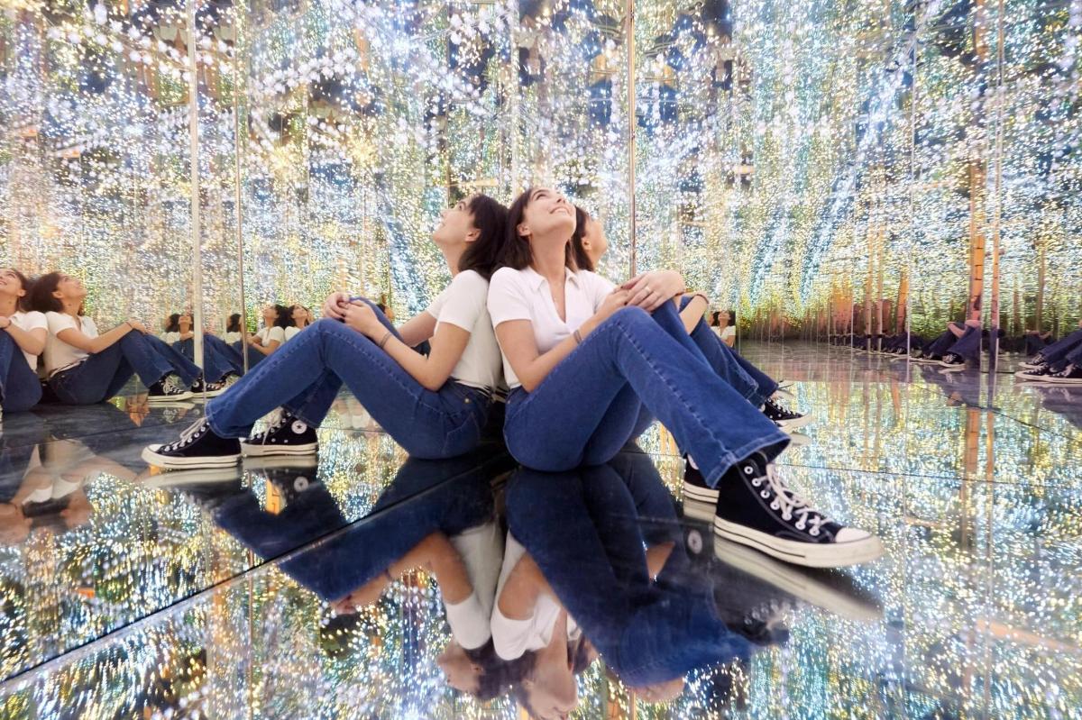 two women sitting on the ground in front of a waterfall