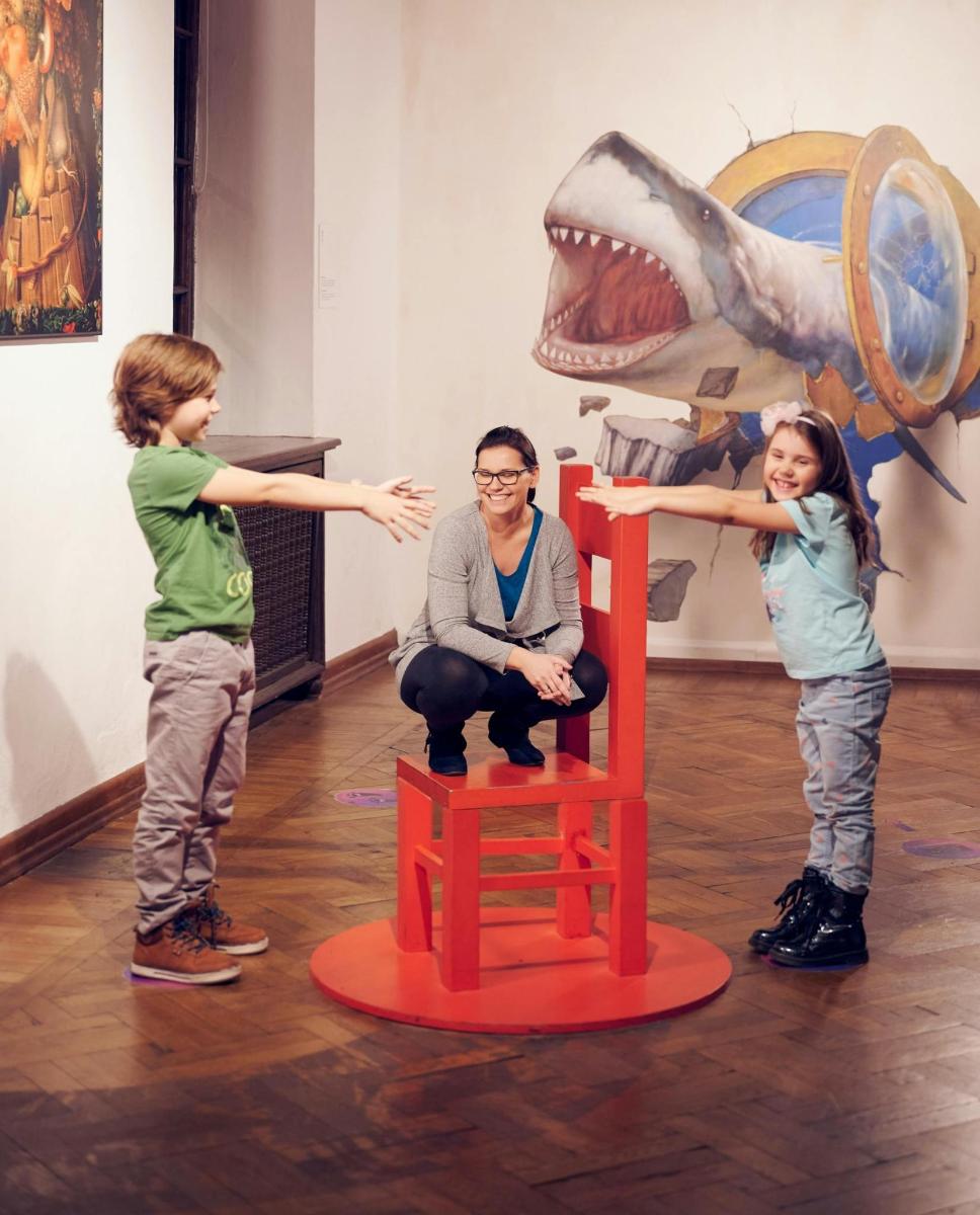 two children and a man playing with a toy with a shark on a chair
