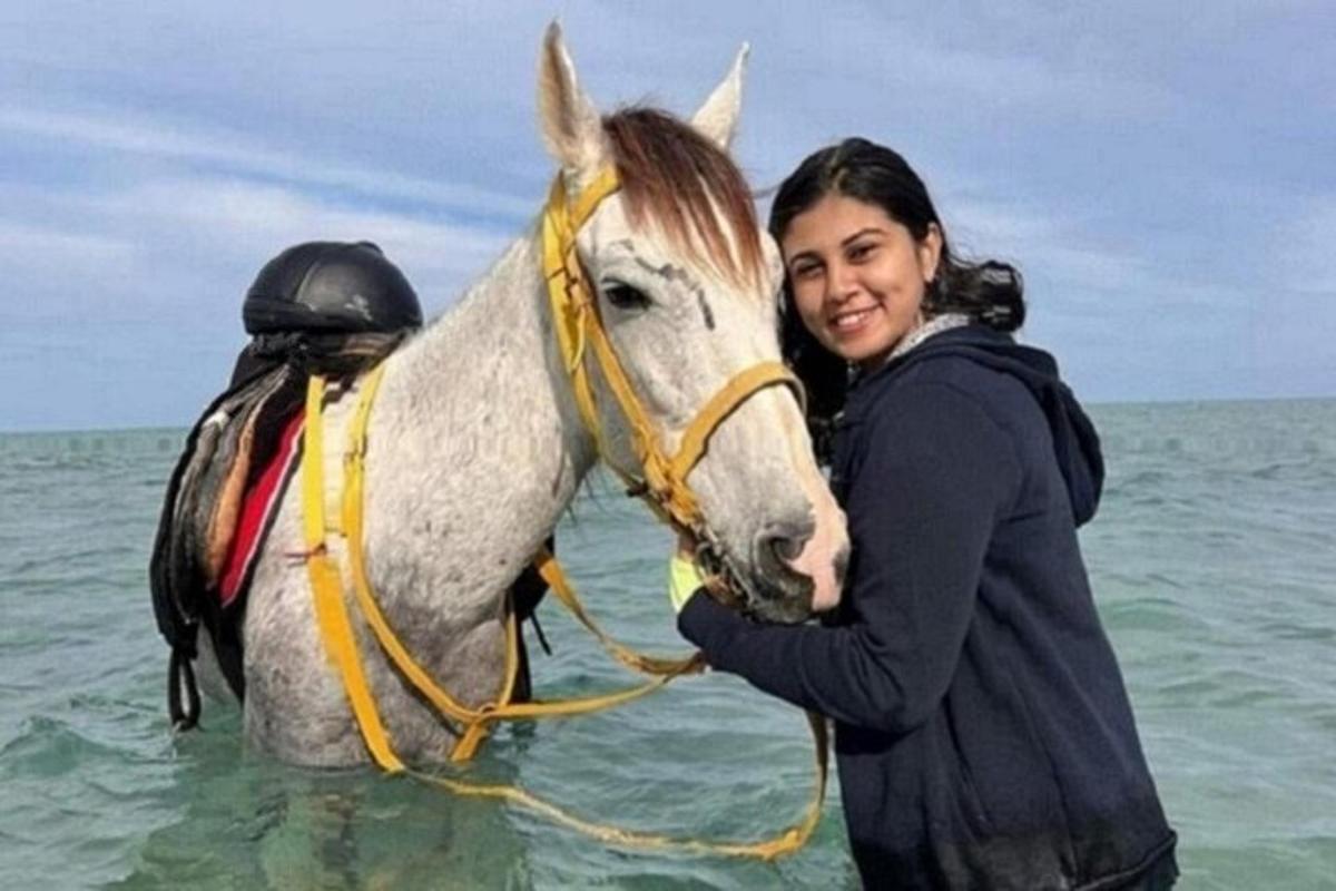 žena stojící vedle koně v oceánu