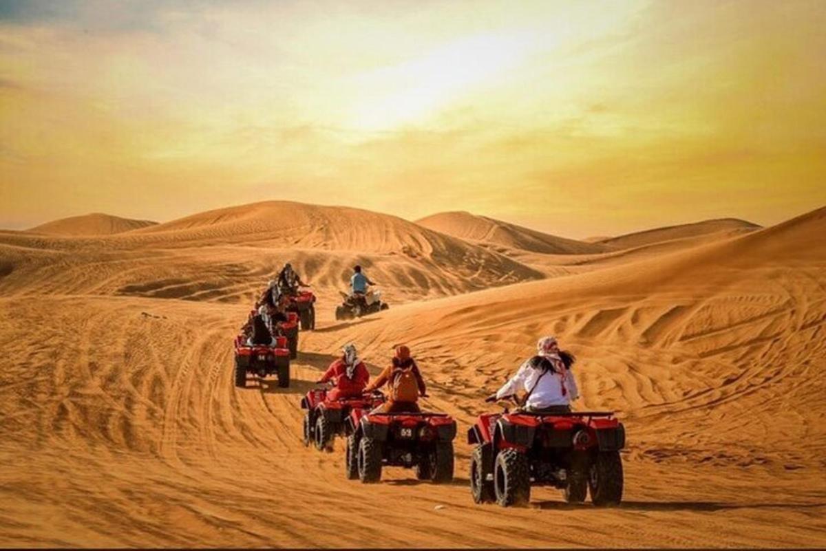 sekumpulan orang menunggang basikal quad di padang pasir