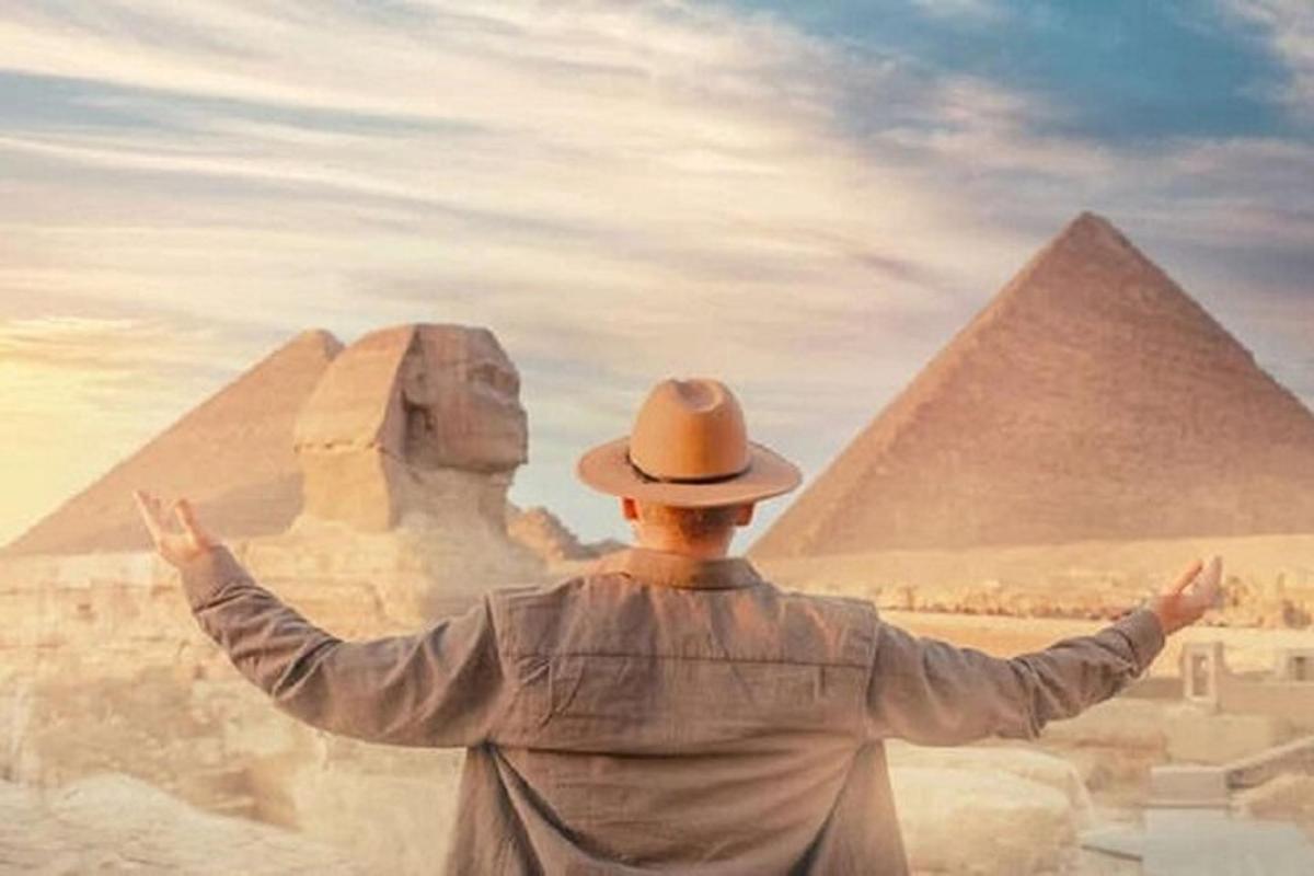 a man in a hat standing in front of the pyramids