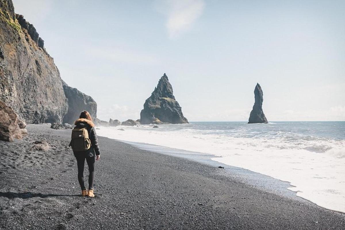 a woman walking on the beach with two rocks in the ocean