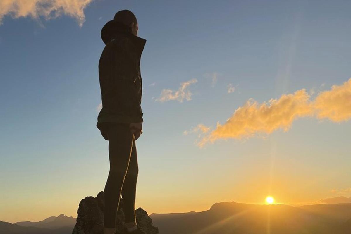 una persona dempeus al cim d'una muntanya a la posta de sol