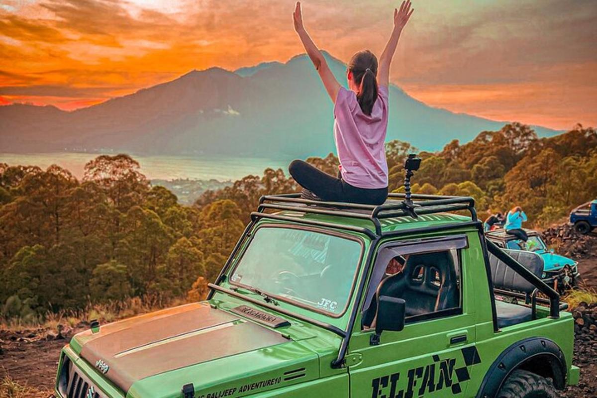une femme assise sur une voiture verte avec les bras levés