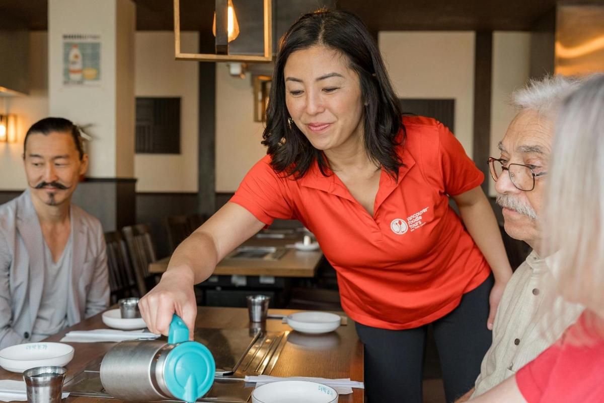 Una mujer parada en una cocina con dos personas mayores.