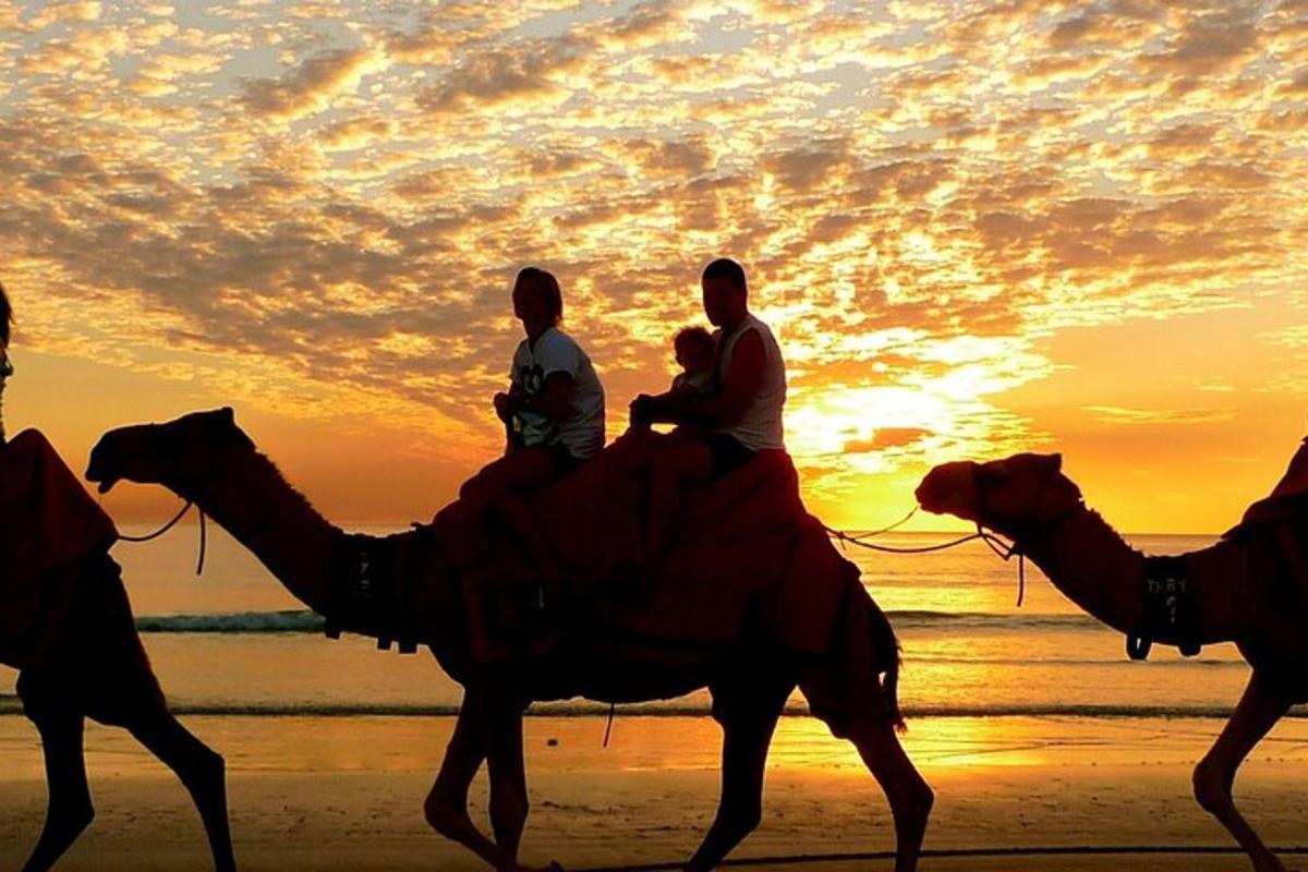 un gruppo di persone a cavallo di cammelli sulla spiaggia al tramonto