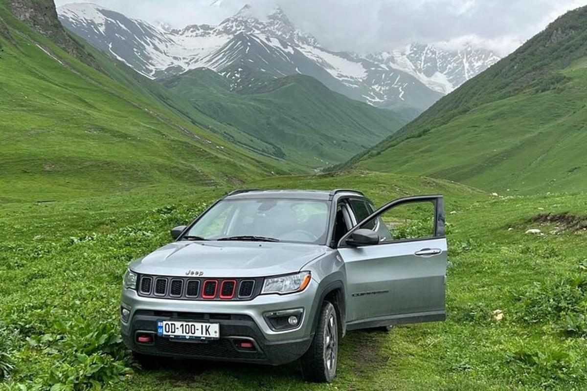 isang silver jeep na nakaparada sa isang bukid na may mga bundok