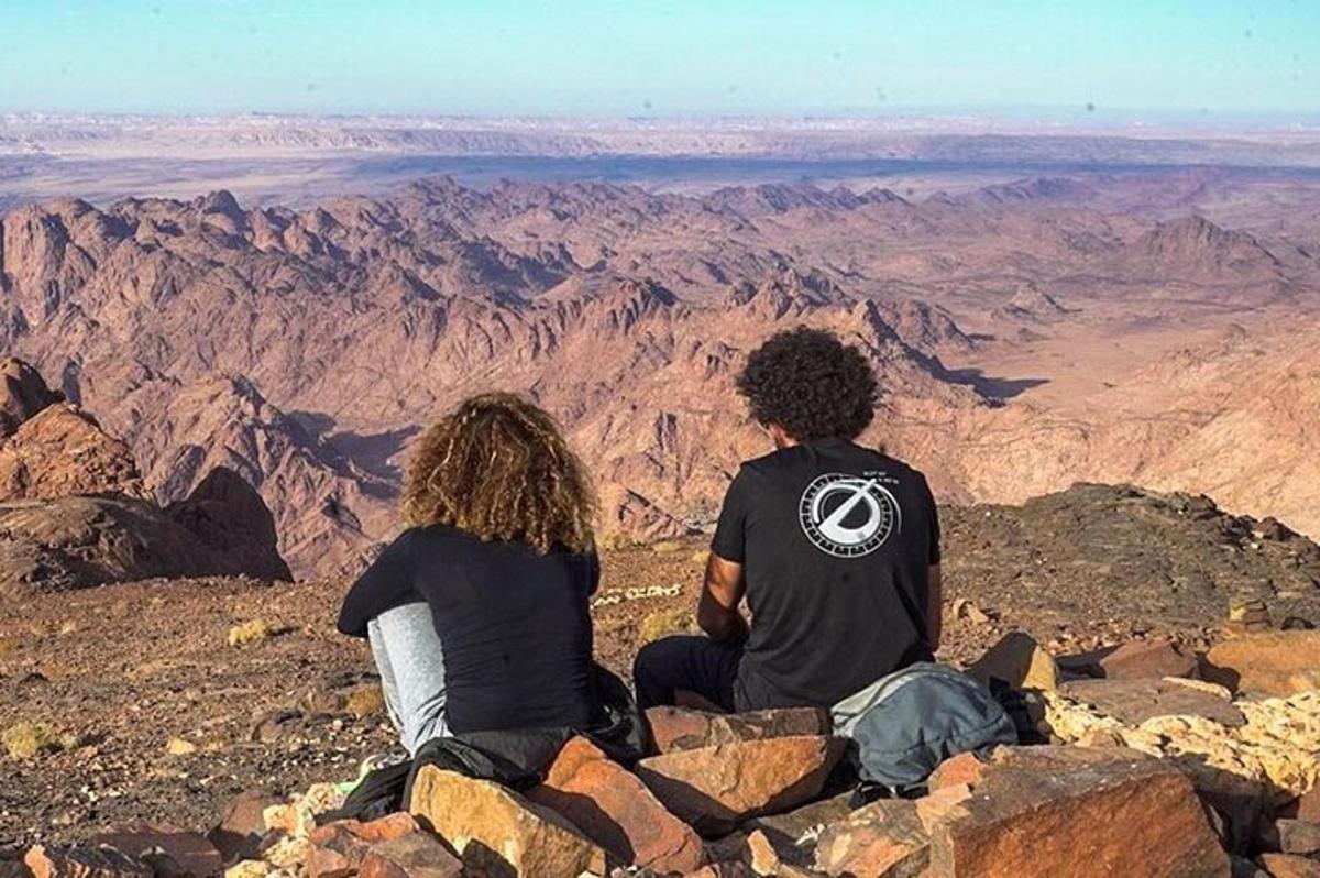 duas pessoas sentadas no topo de uma montanha olhando para o deserto