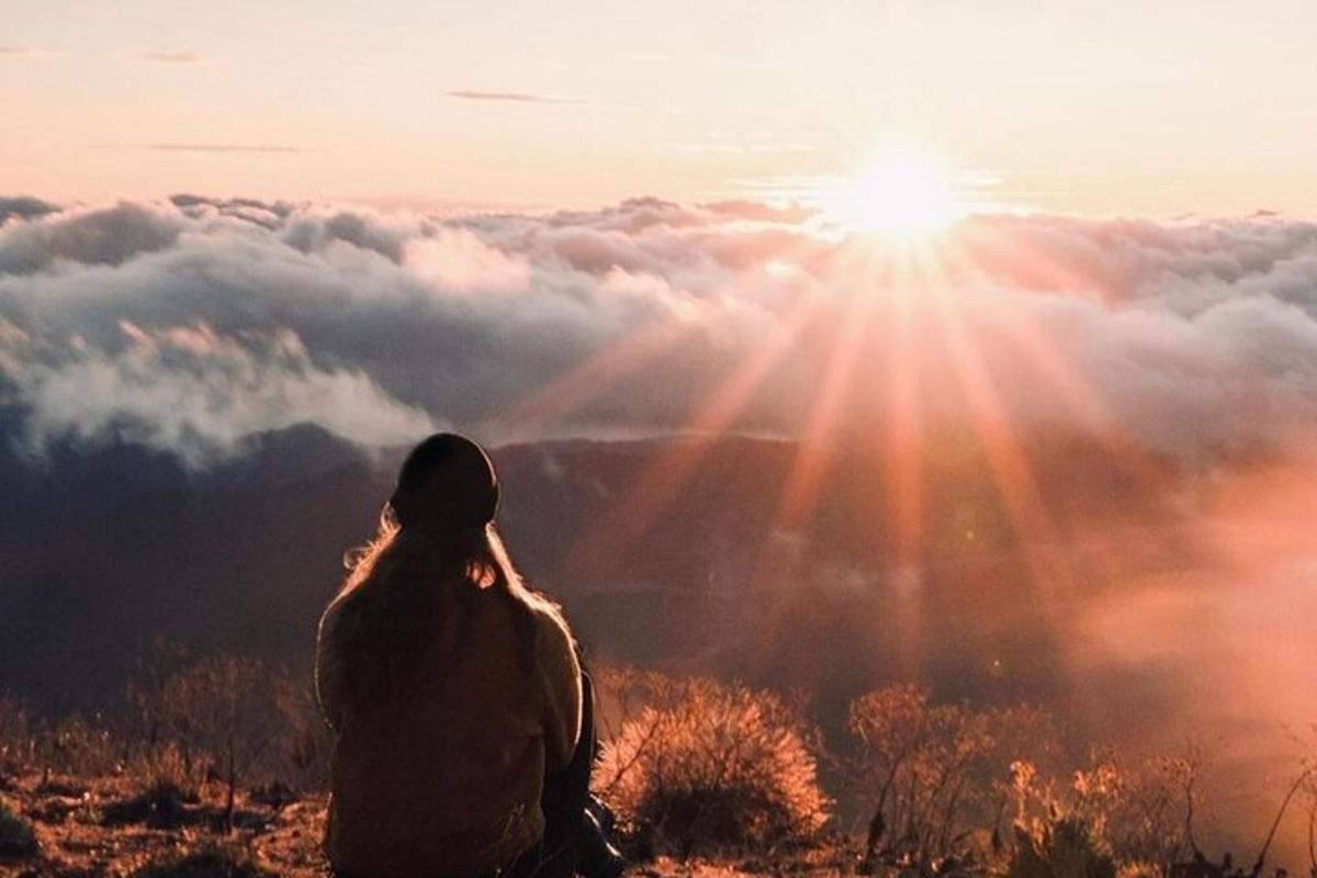una donna seduta in cima a una montagna che guarda il tramonto