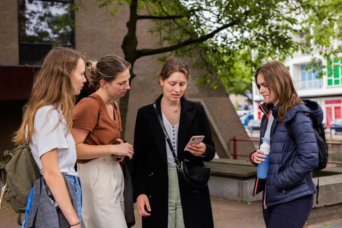 čtyři ženy postávají a dívají se na mobilní telefon