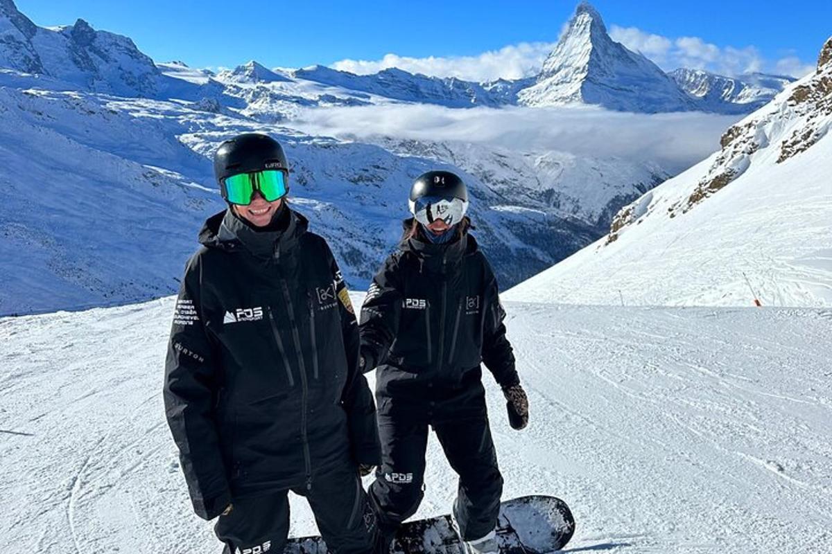 two people standing on a snowboard on a mountain