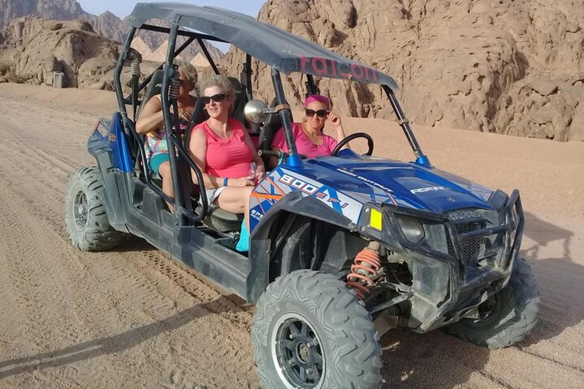 três pessoas sentadas em um quadriciclo no deserto