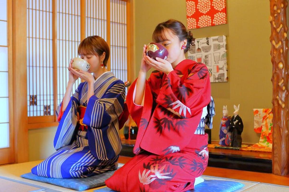 two young girls in kimonos sitting on the floor drinking from donuts
