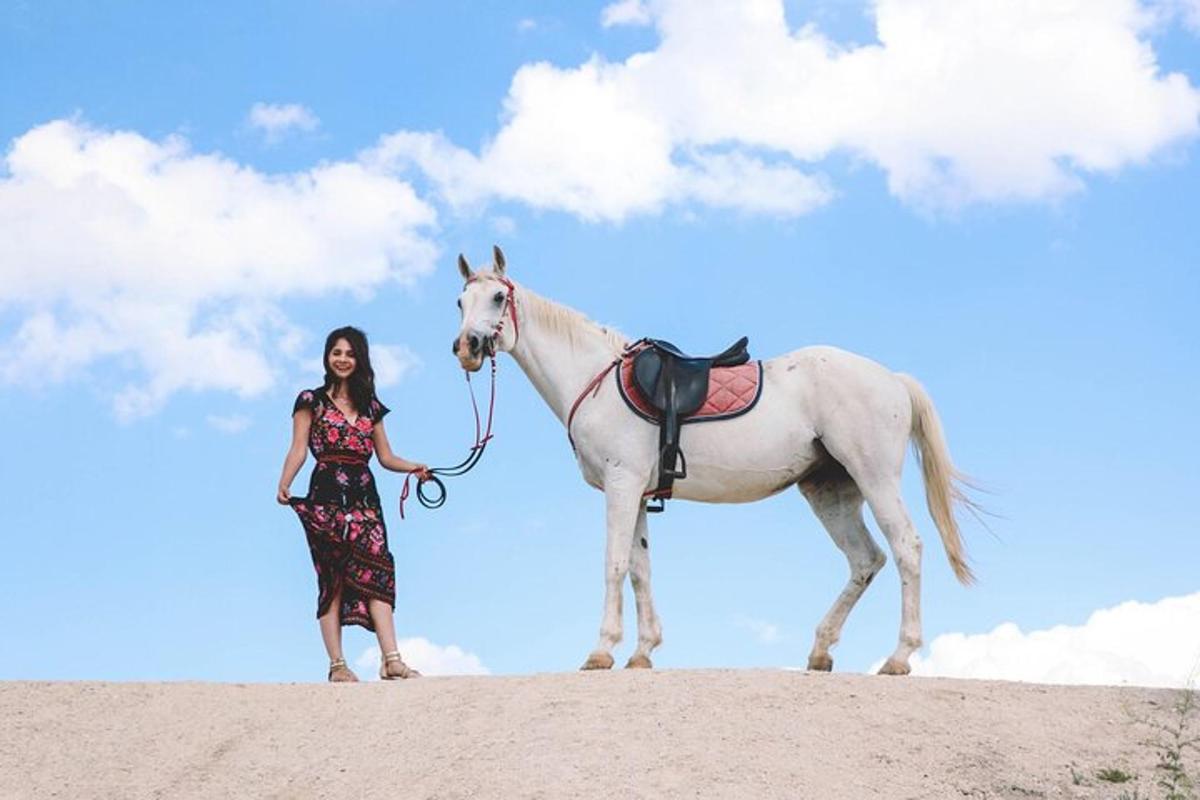 uma mulher parada ao lado de um cavalo branco em uma colina