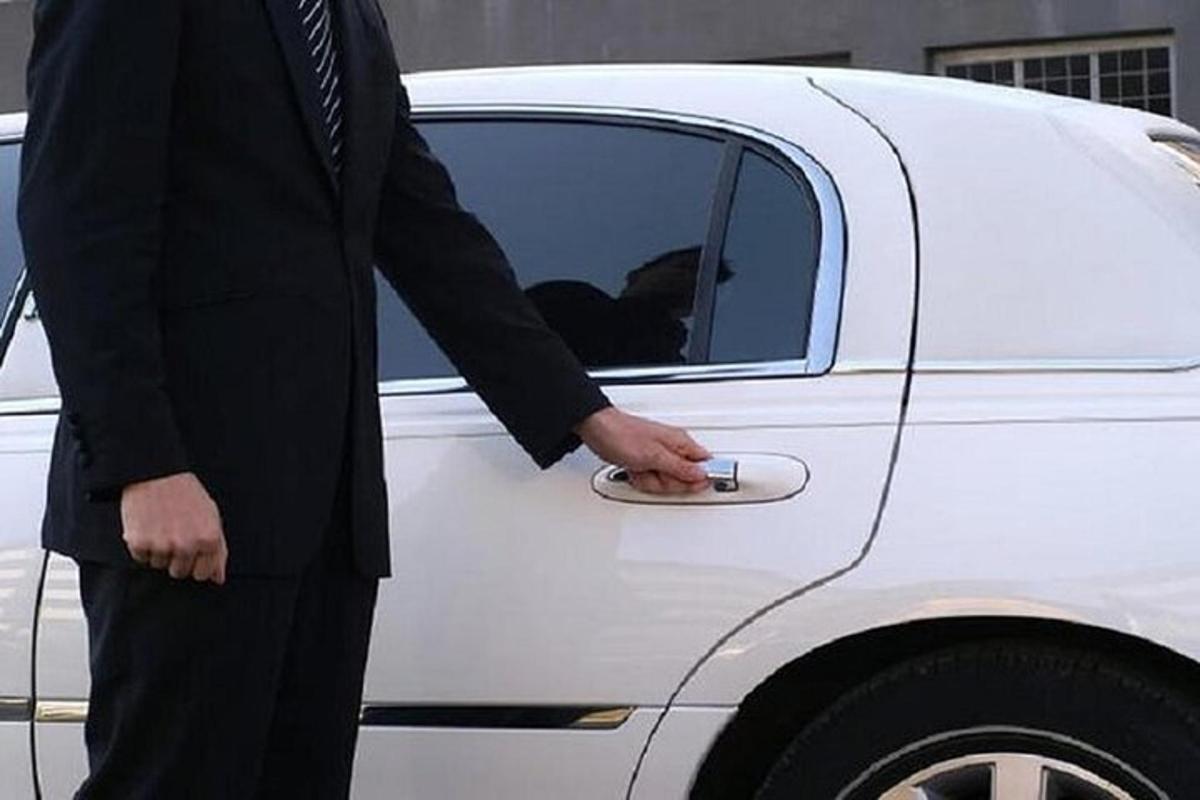 seorang lelaki berpakaian sut berdiri di sebelah kereta putih