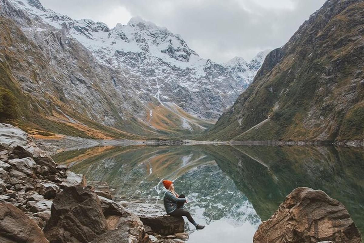 a person sitting on a rock near a mountain lake