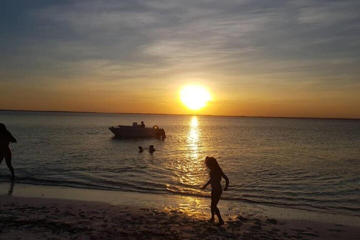 a group of people walking on the beach with a boat in the water