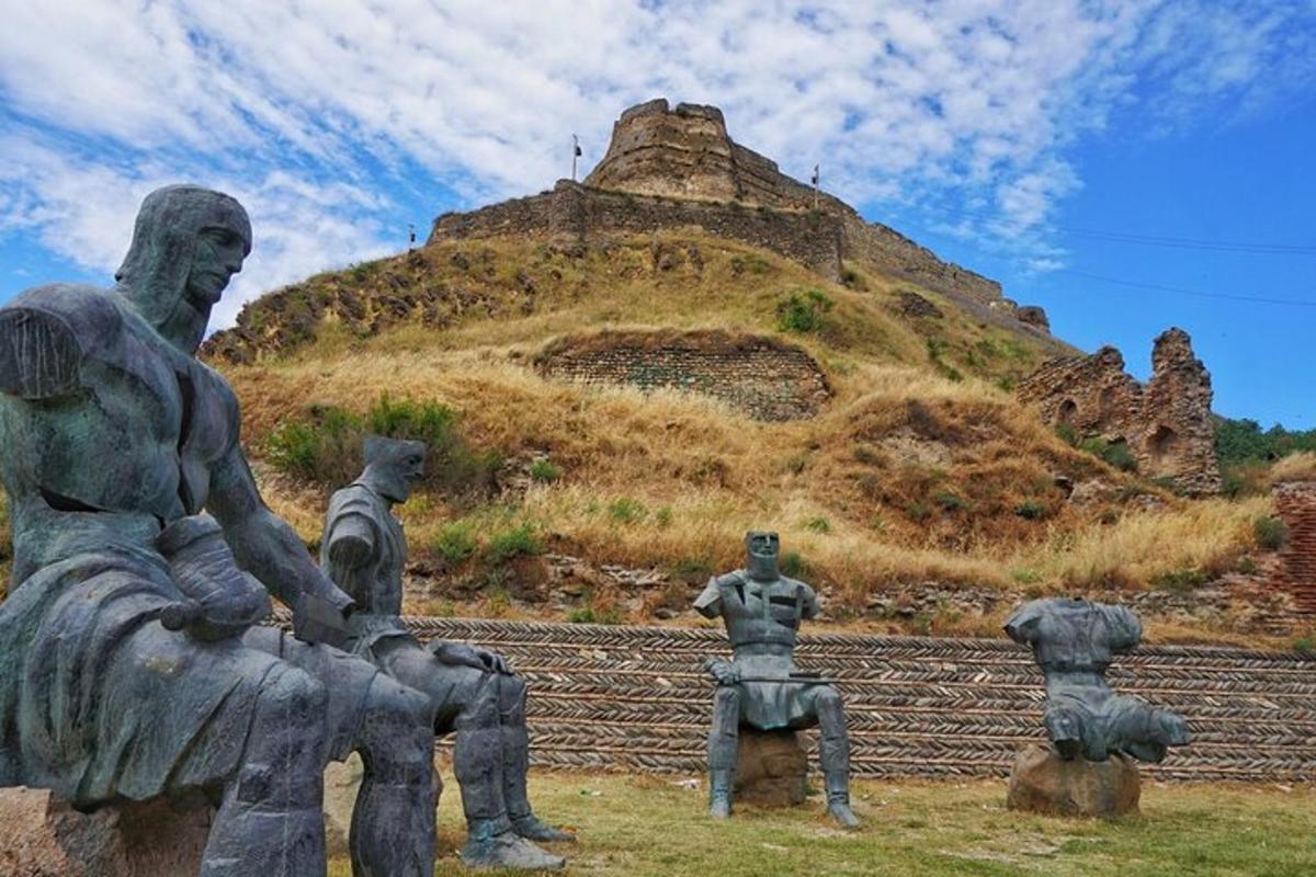 Una estatua de personas sentadas en un banco frente a una montaña.