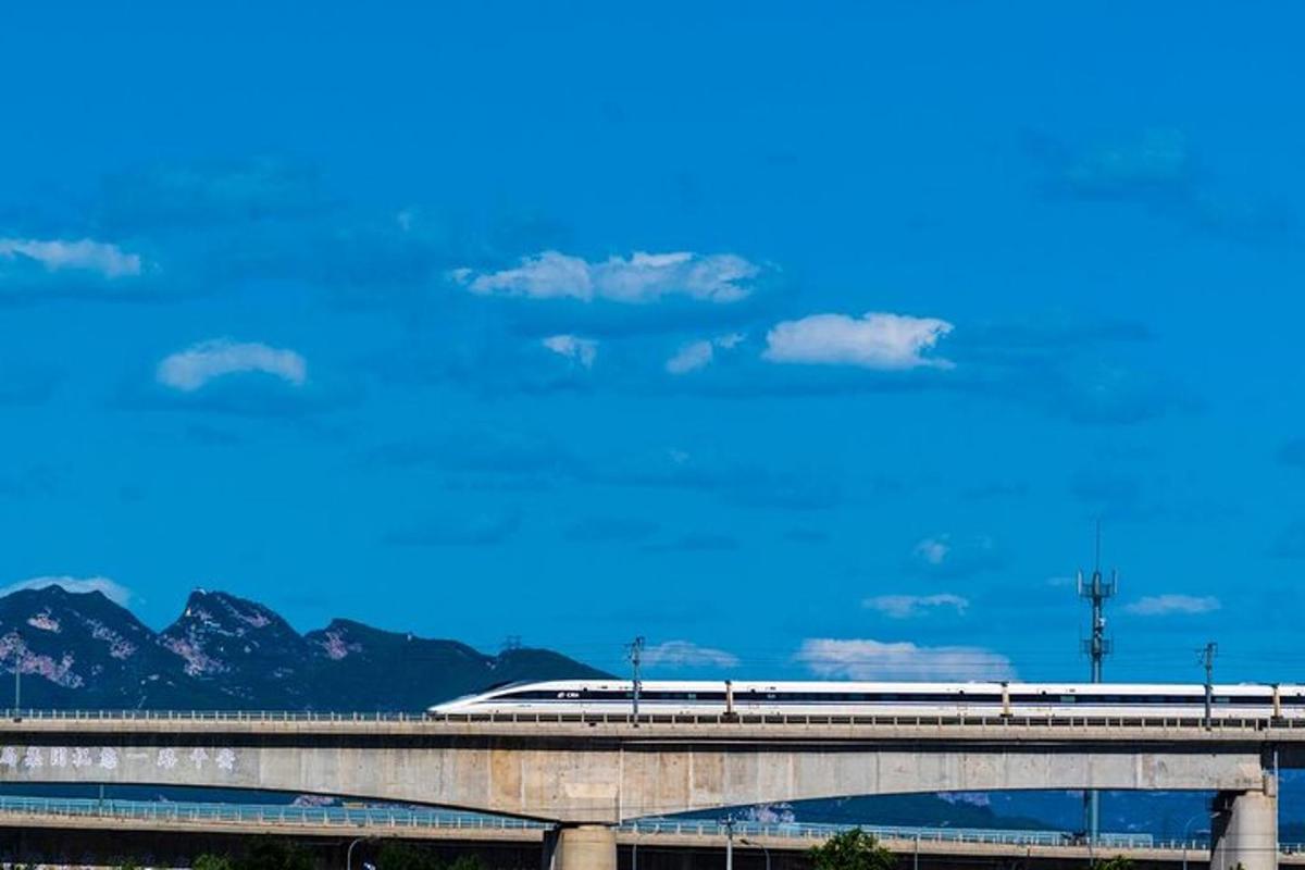 a train on a bridge with a blue sky and mountains