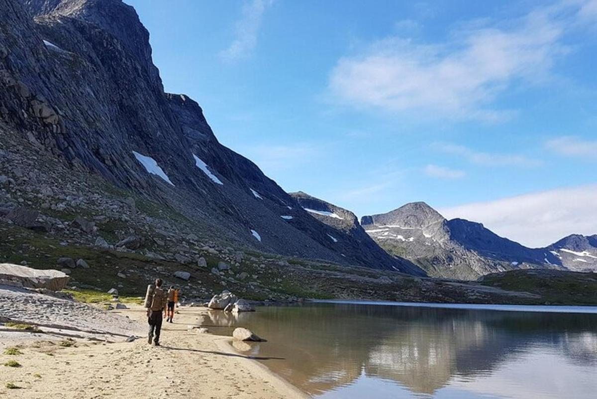 two people walking on a beach near a mountain lake