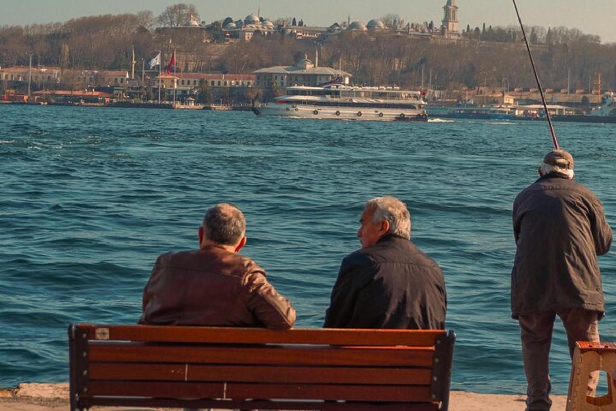 Τρεις άντρες κάθονται σε ένα παγκάκι κοιτάζοντας το νερό