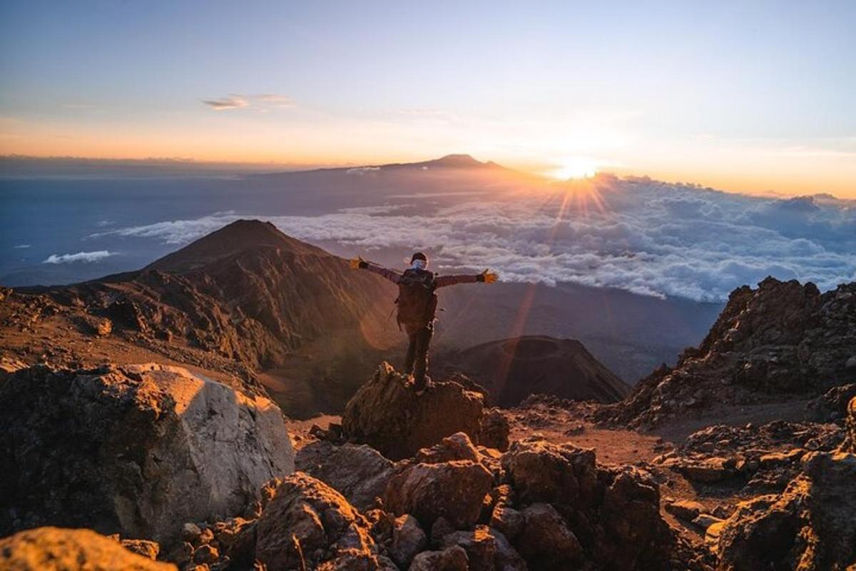 Un hombre parado en la cima de una montaña con los brazos extendidos.