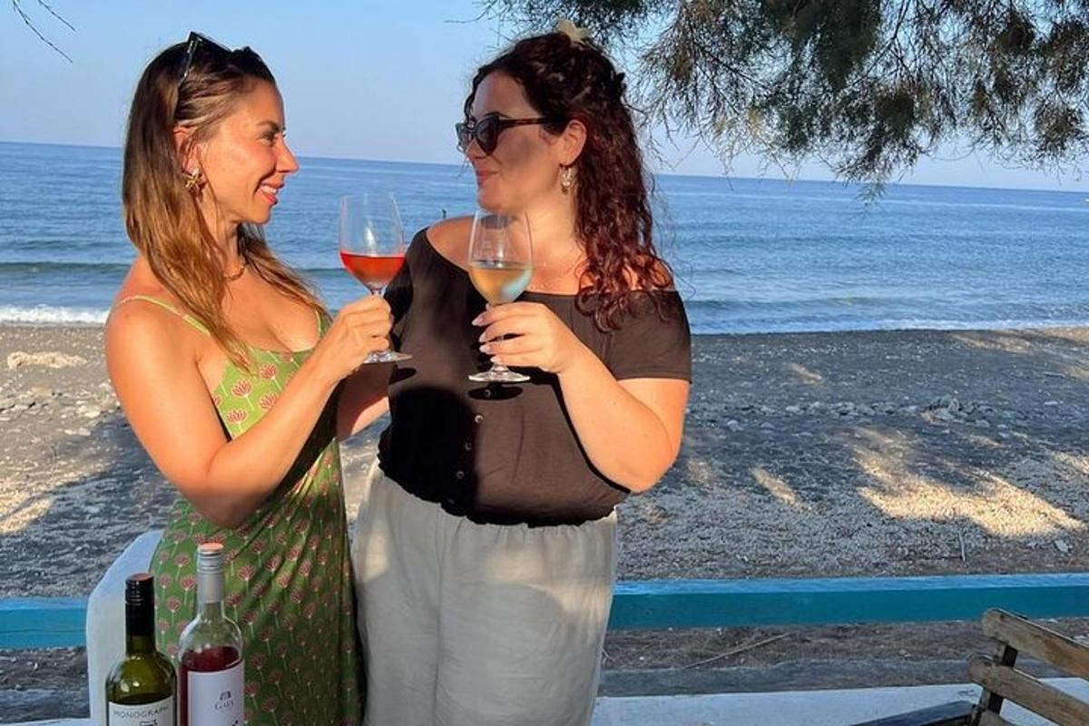 dua wanita berdiri di pantai sambil memegang gelas anggur