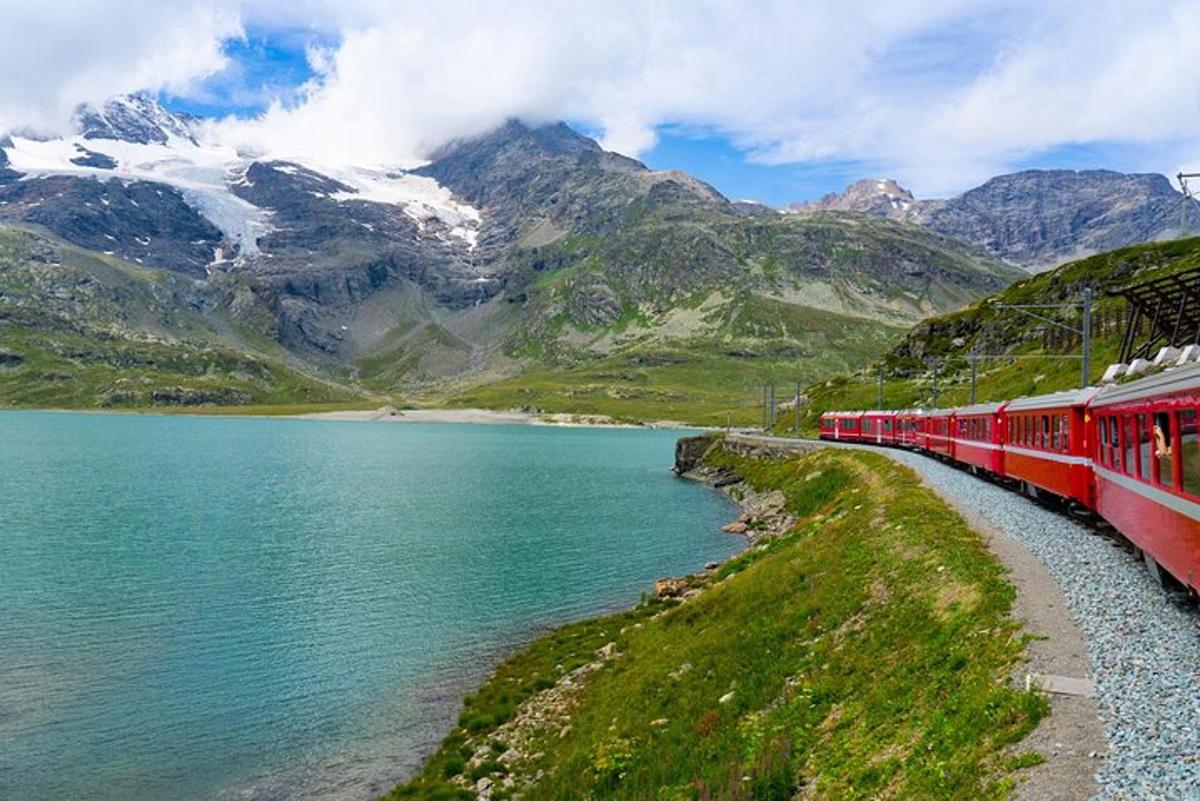 a red train traveling through the mountains next to a lake