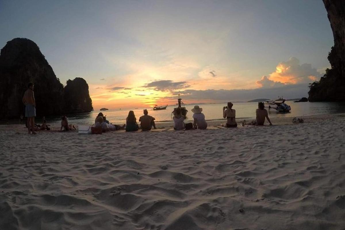 um grupo de pessoas sentadas na praia assistindo ao pôr do sol