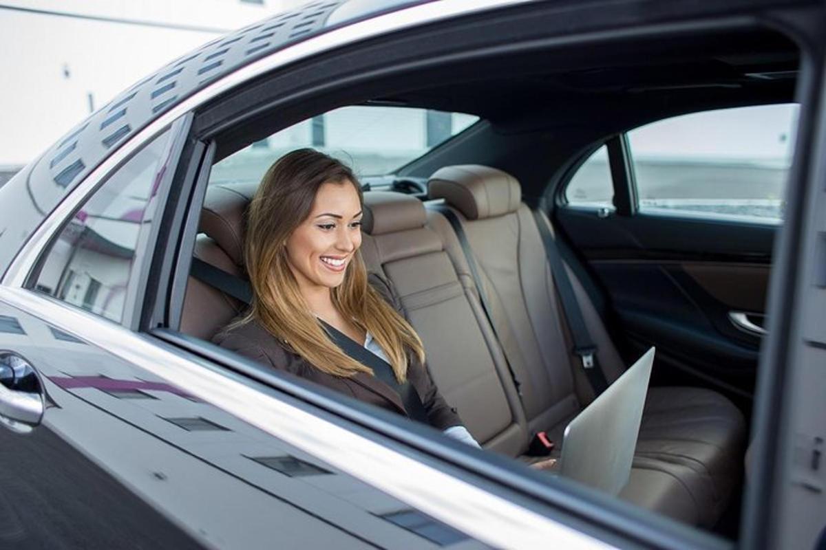 Una mujer sentada en el asiento trasero de un automóvil con una computadora portátil.