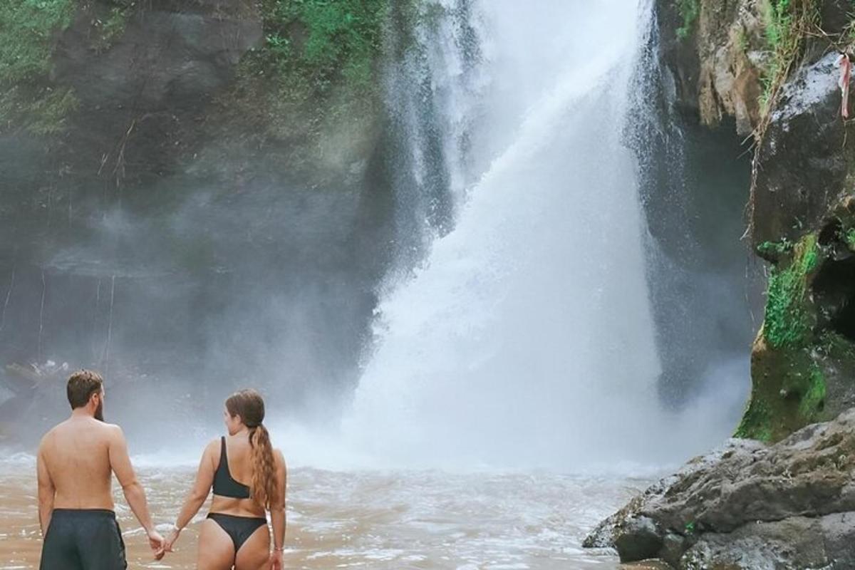 um homem e uma mulher parados na água em frente a uma cachoeira