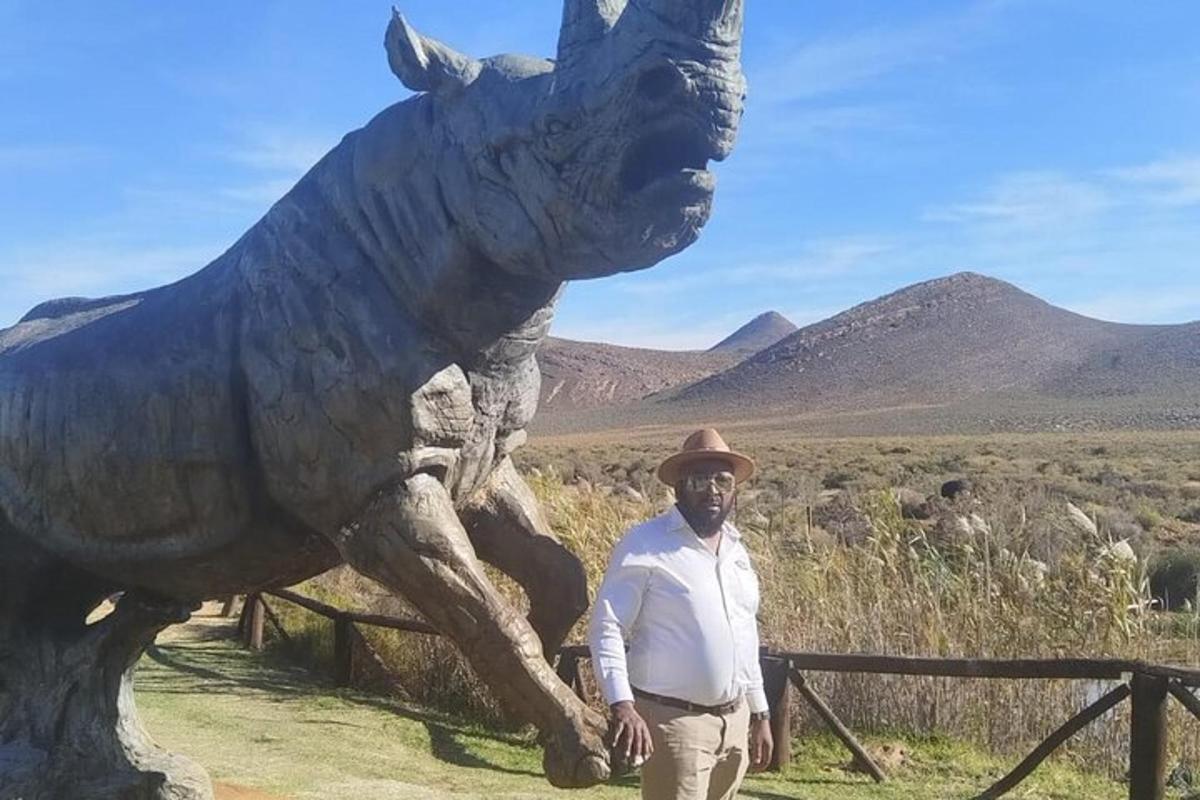 un home dret davant d'una estàtua d'un dinosaure