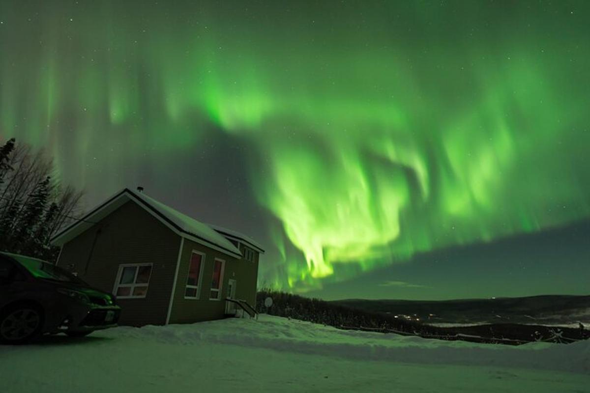 una casa con un'auto parcheggiata nella neve accanto all'aurora