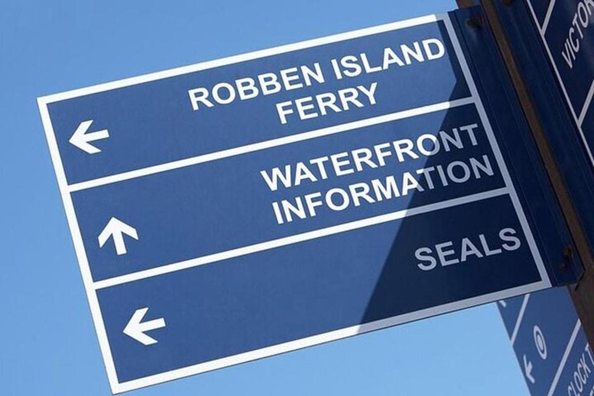 een blauw straatnaambord met de woorden Ribbon Island Ferry en informatiezegels over de waterkant