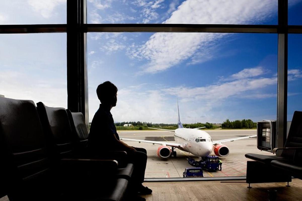 maður situr í flugstöð og horfir á flugvél