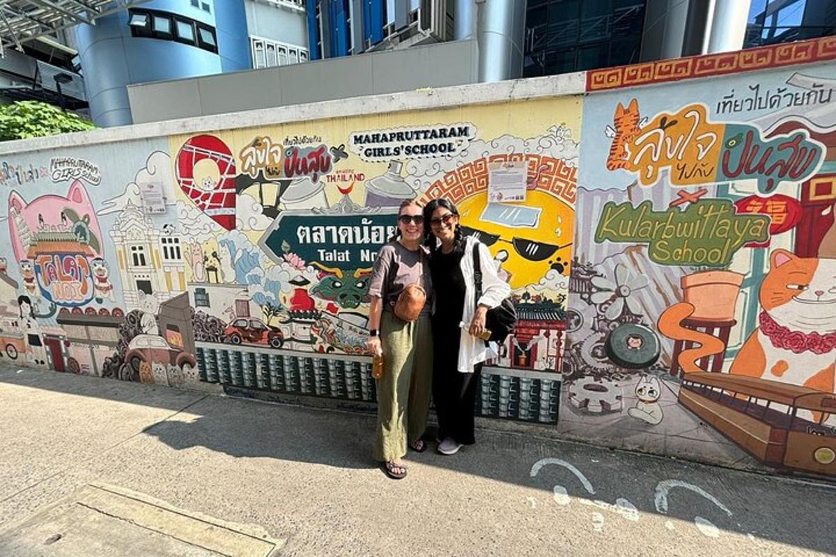 duas pessoas em pé em frente a uma parede com um mural