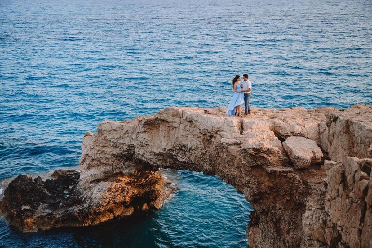 um casal em pé sobre uma formação rochosa no oceano