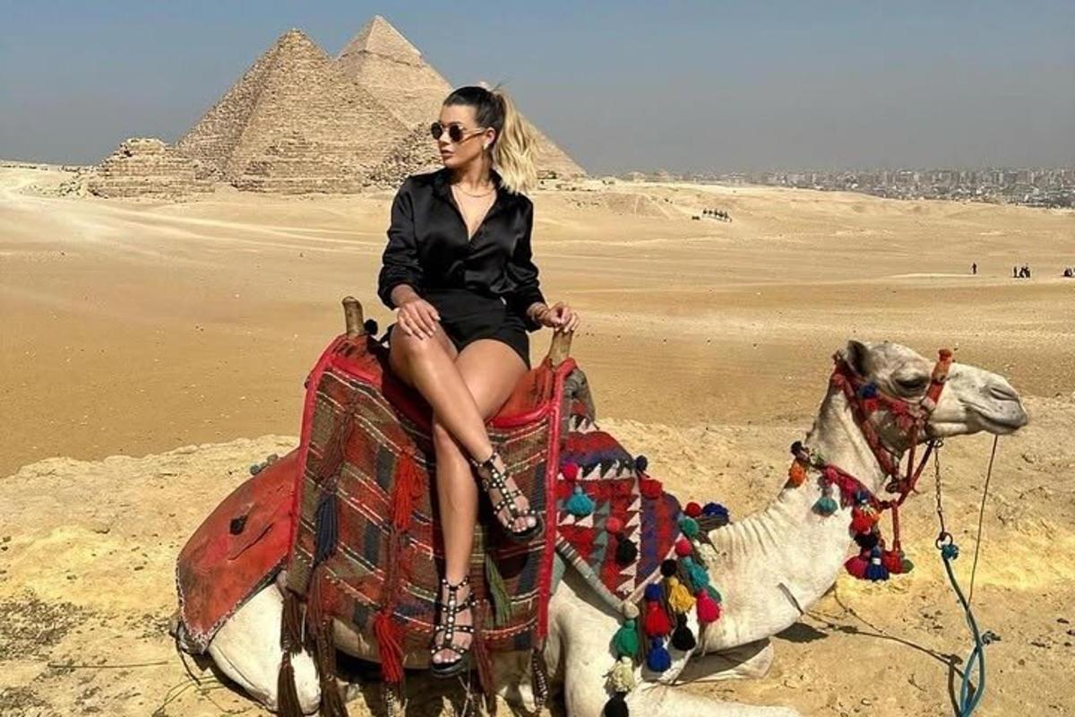 egy nő tevén ül a piramisok előtt