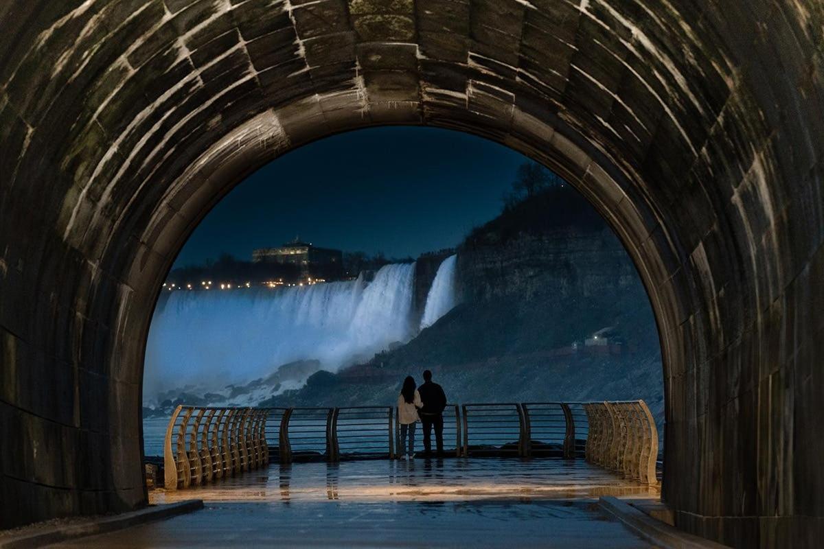 two people standing under a tunnel looking at a waterfall