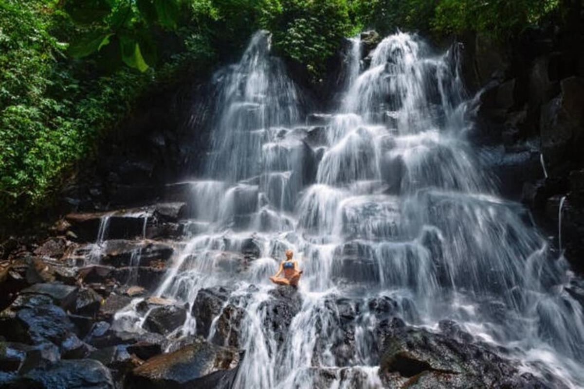 una persona seduta su una roccia di fronte a una cascata