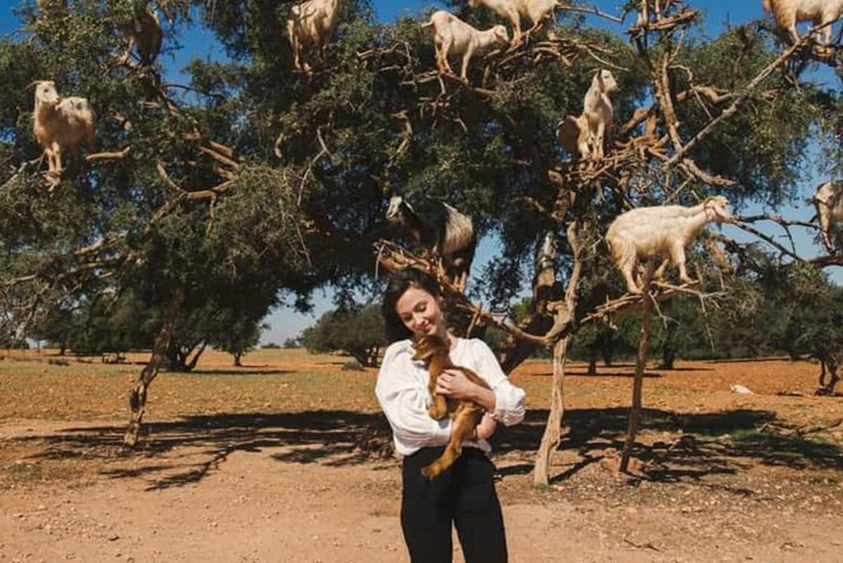 a woman holding a dog in front of a tree with goats