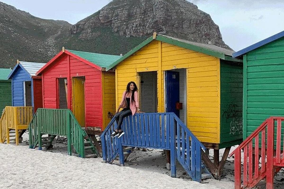a woman sitting on a bench in front of colorful beach huts